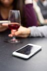 Femme utilisant un smartphone près d'un verre de vin — Photo de stock