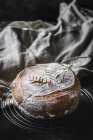 Loaf of fresh bread loaf on grating with cloth on dark background — Stock Photo