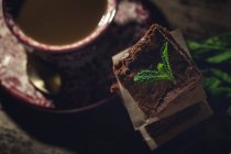 Складені шматочки шоколадного брауні з м'ятою на темному фоні з чашкою кави — стокове фото