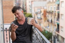 Relaxing man having coffee and browsing phone on balcony — Stock Photo