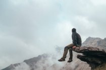 Чоловік сидить на скелі біля гори між хмарами — стокове фото
