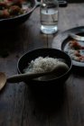 Миска рису і порожня тарілка на сільському дерев'яному столі на темному фоні — стокове фото