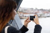 Vista lateral jovem senhora segurando telefone celular e atirando água entre a cidade da ponte no Porto, Portugal — Fotografia de Stock
