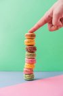 Person hand with showing finger on pile of fresh tasty macarons on blue board on green background — Stock Photo
