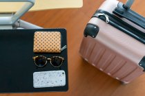From above rose plastic luggage bag with handle near seat with table with sunglasses, purse and mobile phone in Porto, Portugal — Stock Photo