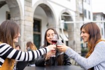 Attraktive lächelnde Damen klimpern mit Weingläsern am Tisch eines Straßencafés in Porto, Portugal — Stockfoto