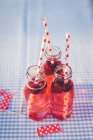 Flaschen mit frischem Fruchtgetränk und Trinkhalmen auf karierter Tischdecke — Stockfoto