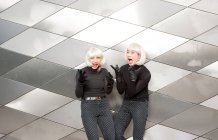 Blond smiling ladies in same cloths posing near wall — Stock Photo