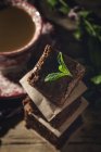Stacked pieces of chocolate brownie with mint on dark background with cup of coffee — Stock Photo