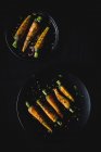 Healthy roasted carrots with herbs and spices on black plates on dark background — Stock Photo