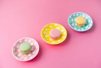Dall'alto brillanti deliziosi macarons su piatti su sfondo rosa — Foto stock