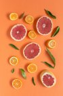 Мандарин и грейпфрутовый ломтик с зелеными листьями на оранжевом фоне — стоковое фото