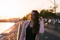 Giovane ragazza con la mano nei capelli che cammina sul vicolo al tramonto — Foto stock