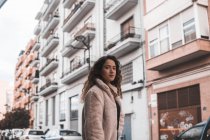 Серйозна молода жінка з кучерявим волоссям дивиться на камеру, стоячи на міській вулиці — стокове фото