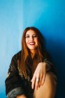 Усміхнена приваблива жінка сидить у синій стіні — стокове фото