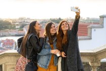 Stylisch attraktive, lächelnde Damen in Freizeitkleidung machen ein Selfie auf dem Smartphone vor dem Hintergrund der Stadtlandschaft in Porto, Portugal — Stockfoto