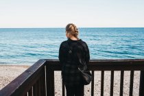 Vista posteriore della giovane donna in abito casual in piedi vicino ringhiera su argine e ammirando vista sul mare meraviglioso di Altea, Spagna — Foto stock