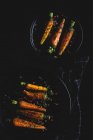 Zanahorias asadas saludables con hierbas y especias en platos negros sobre fondo oscuro - foto de stock