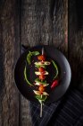 Макароны с помидорами и базиликом на палочке на черной тарелке с соусом на темной древесине — стоковое фото