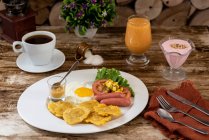 Сніданок з яйцями і ковбасою на тарілці і чашкою кави, розміщеної поруч на дерев'яному столі в кафе — стокове фото