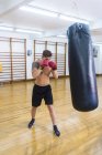 Молодой бородатый парень тренируется в спортзале с боксерской грушей — стоковое фото