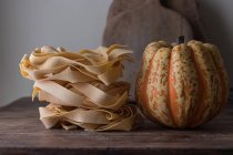 Un mucchio di spaghetti di pappardelle crude e zucca fresca sul tavolo di legno — Foto stock