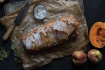 Homemade pumpkin and apple strudel on parchment with ingredients on dark background — Stock Photo