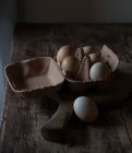 Коробка со свежими куриными яйцами, лежащая на разделочной доске на деревянном столе в темной комнате — стоковое фото