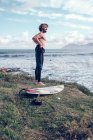 Молодий чоловік з дошкою для серфінгу одягає гідрокостюм біля океану — стокове фото