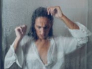 Jolie jeune femme en chemise mouillée blanche debout près du verre de cabine de douche — Photo de stock
