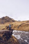 Tipo vista lateral de pie en piedra cerca de río corriente entre montañas marrones en Islandia - foto de stock