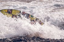 Luminosa tavola da surf in onde e spruzzi di mare vicino alla costa rocciosa — Foto stock