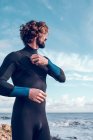 Young bearded man putting on wetsuit near ocean — Stock Photo