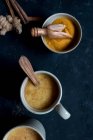 Schalen mit Gewürzen und Tassen mit gewürzten Latte in Tassen auf dunklem Hintergrund — Stockfoto