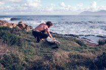 Joven limpiando tabla de surf en la costa del océano - foto de stock