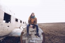 Young lady in warm wear sitting on broken aircraft between dark grounds in Iceland — Stock Photo
