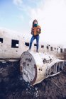 Young lady in warm wear on broken aircraft between dark grounds in Iceland — Stock Photo