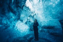 Homme voyageur en tenue debout dans une grotte de glace bleue cristalline levant les yeux, Islande — Photo de stock