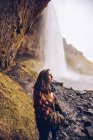 Back view young lady on field near water cascade falling in river between rocks in Iceland — Stock Photo