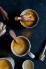 Schalen mit Gewürzen und Tassen mit gewürzten Latte in Tassen auf dunklem Hintergrund — Stockfoto