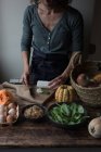 Unrecognizable female cutting ingredients for tasty pumpkin and spinach frittata while standing near wooden table 2maria — Stock Photo