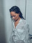 Menina atraente em camisa molhada branca de pé sob spray de água no chuveiro — Fotografia de Stock