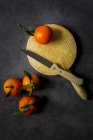 Fresh tangerines with stems and leaves on dark background with wooden board and knife — Stock Photo