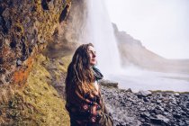 Retour jeune dame sur le terrain près de la cascade d'eau tombant dans la rivière entre les rochers en Islande — Photo de stock