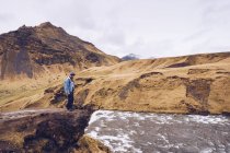 Vista lateral cara de pé na pedra perto de rio de streaming entre montanhas marrons na Islândia — Fotografia de Stock