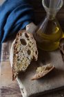 Fetta di pane integrale su tagliere rustico in legno con bottiglia di olio — Foto stock