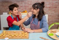 Mamá e hijo jugando con masa y harina mientras trabajan en pastelería en casa - foto de stock