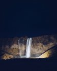 Beleuchtete Wasserkaskade stürzt in der Dunkelheit in Island zwischen Felsen — Stockfoto