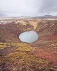 Desde arriba lago en el cráter entre la muerte tierras marrones y colinas con nubes en Islandia - foto de stock