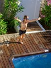 Сверху снимок смешного мальчика в плавательных шортах и очках, бегущего по бассейну к чистой воде и кричащего от волнения — стоковое фото